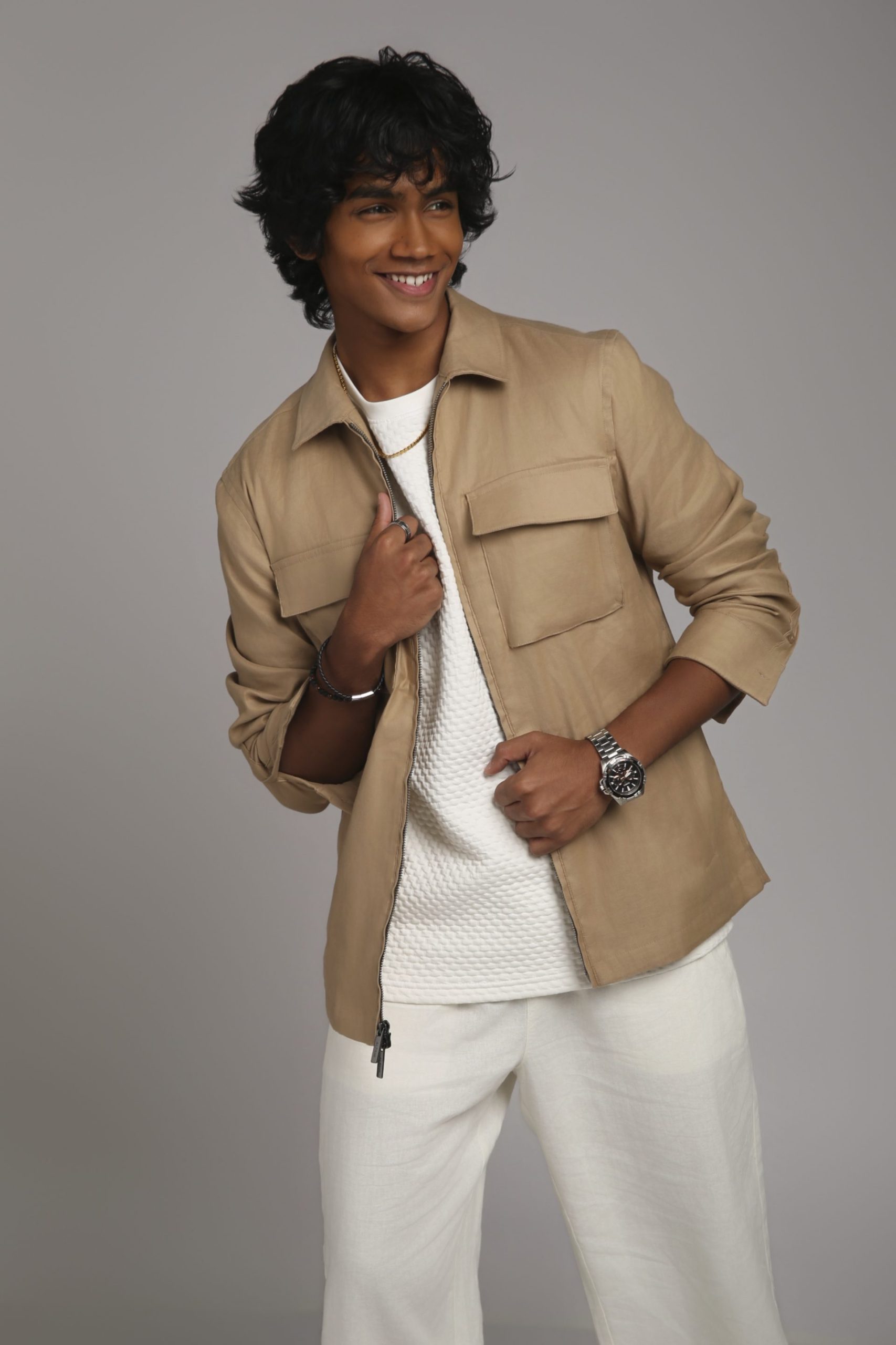 Shabs standing in a beige overshirt and white trousers