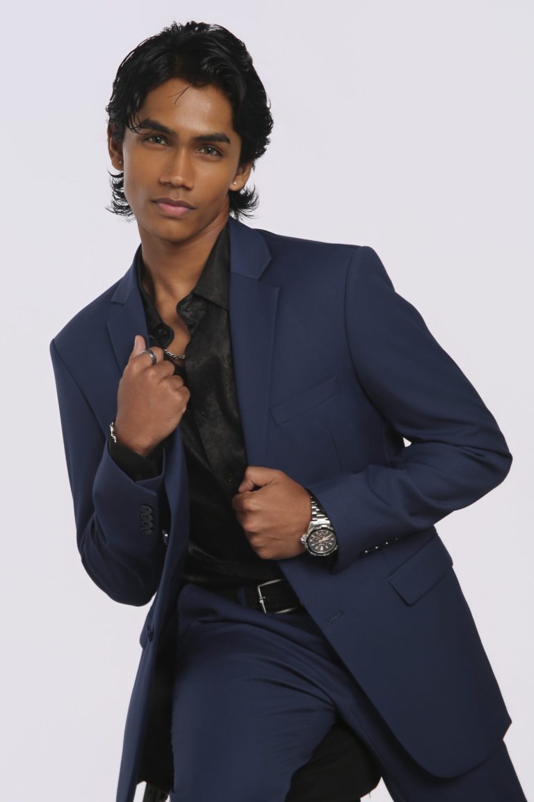 Shabs in a navy suit holding the lapels of his jacket