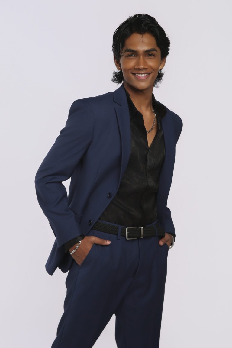 Shabs in a navy suit, hands in pockets, smiling